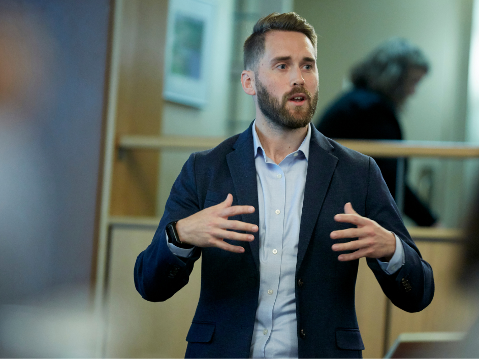 A business professional presenting with expressive hand gestures in front of two people.