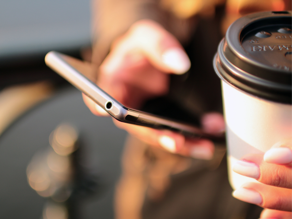 Person holding a smartphone in one hand and a coffee cup in the other.