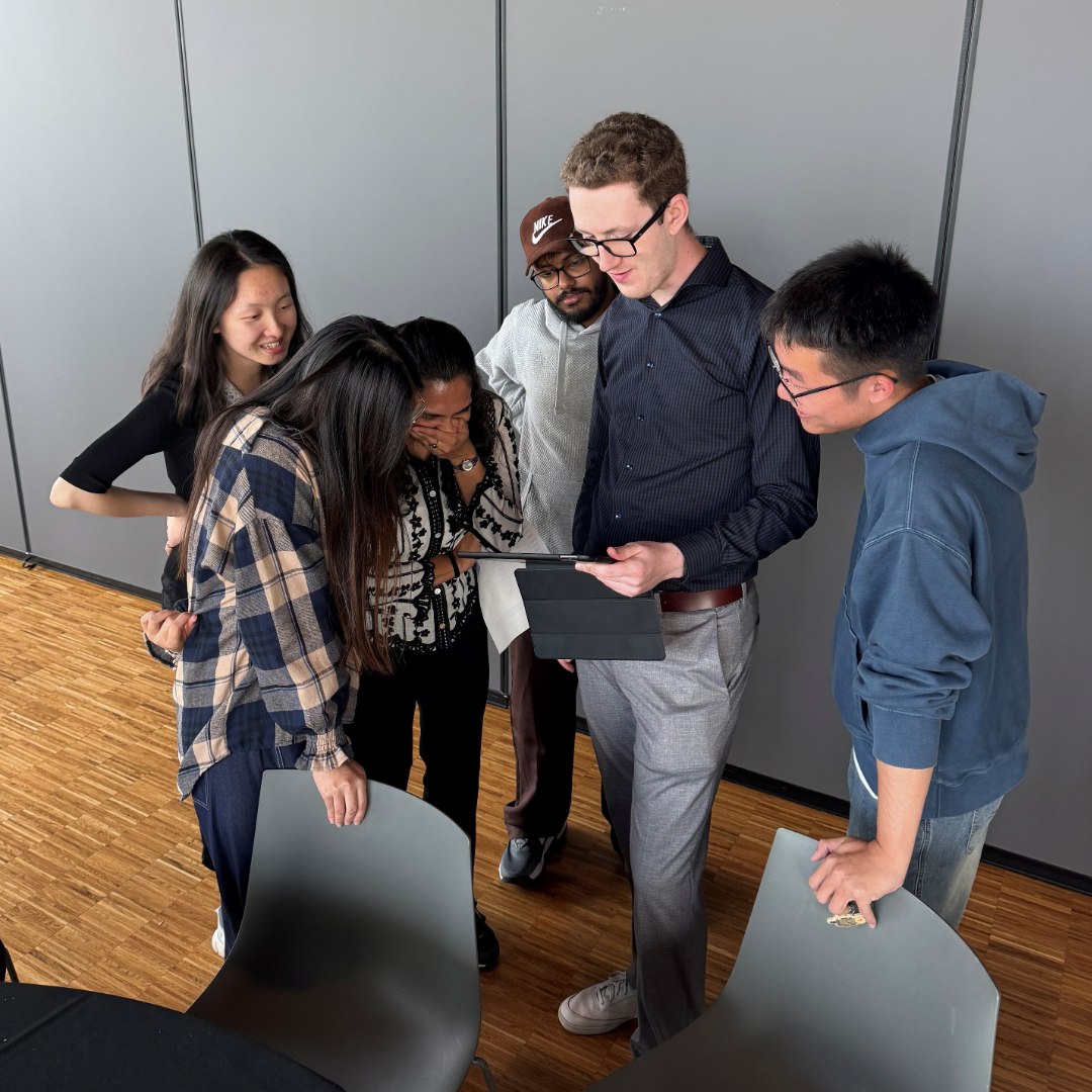 A group of students gather around a faculty member holding a tablet.