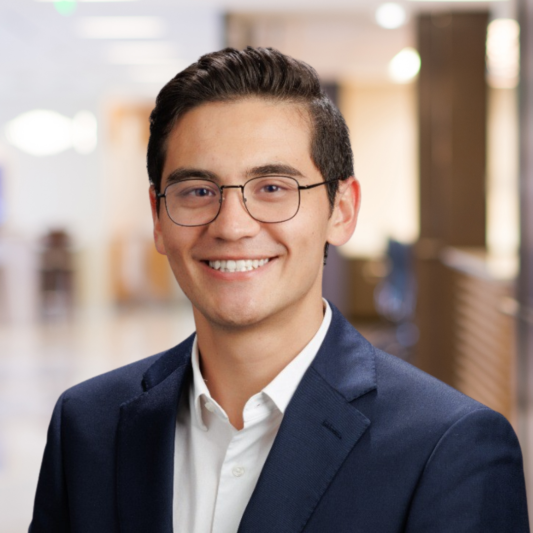 Headshot of Alexander Marks De Chabris, a smiling man wearing glasses and a suit.