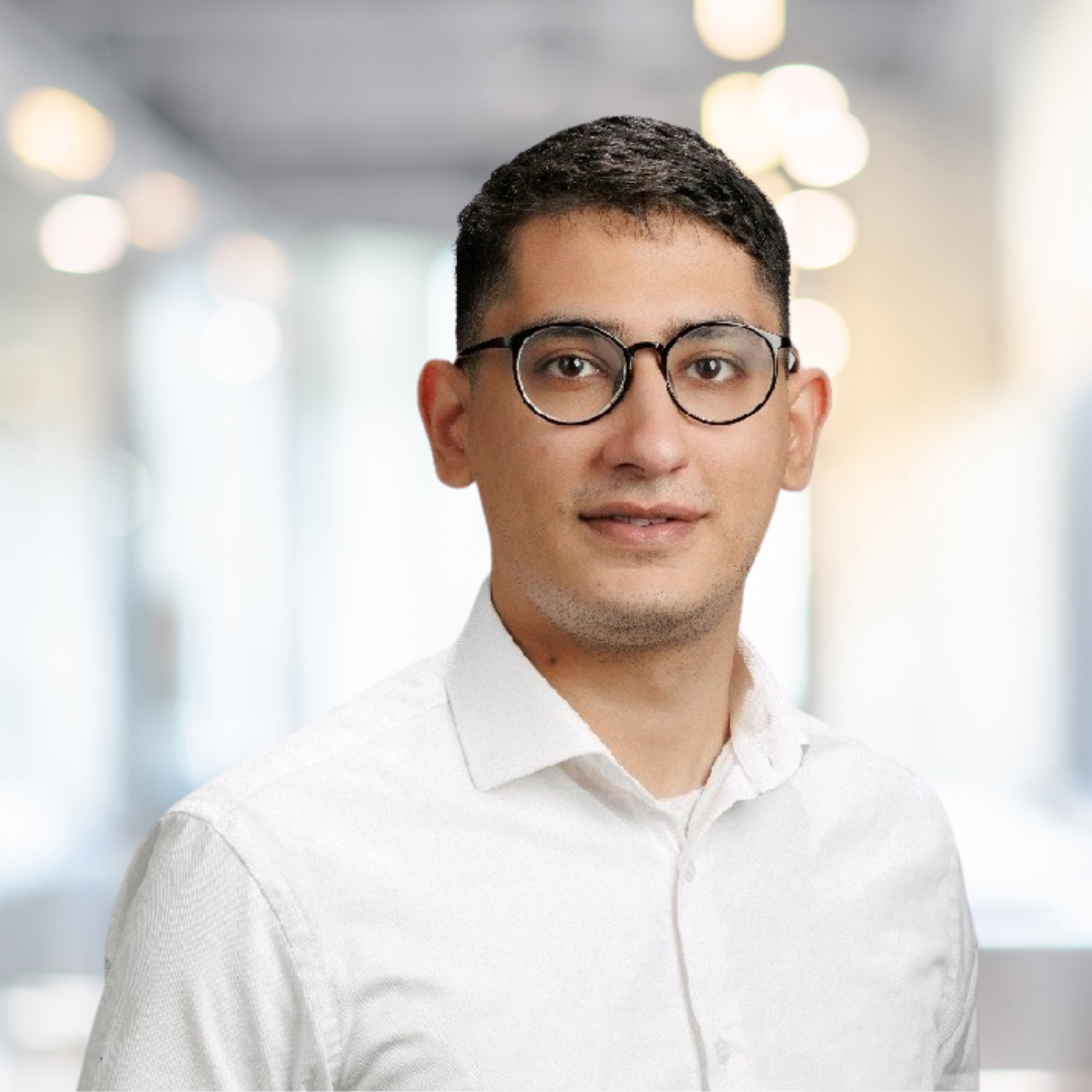 Headshot of Shahzain Bey, a smiling man with short, dark hair, glasses, wearing a white shirt.
