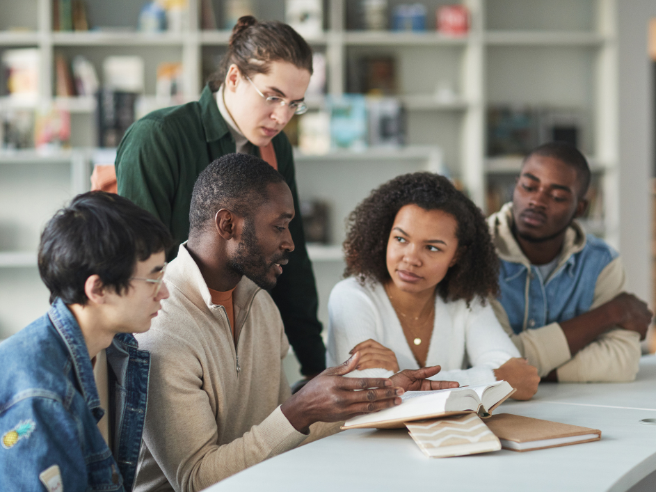 An advisor speaking with four students as they are seated a desk.