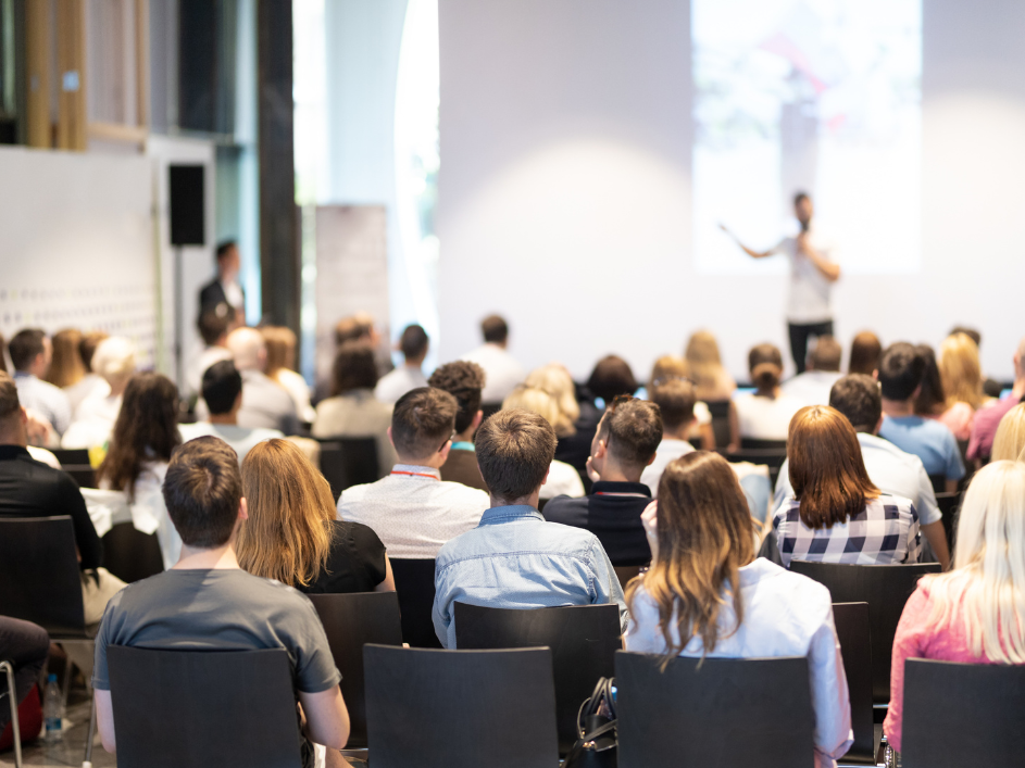 A crowd of seated students listening to a speaker on stage.